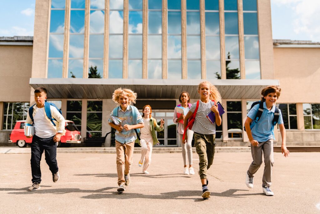 Small kids schoolchildren pupils students running out of the school building after classes